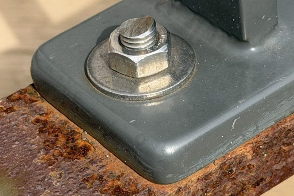 Roestende onderregel van een hekwerk onder een gecoate voetplaat met RVS bout