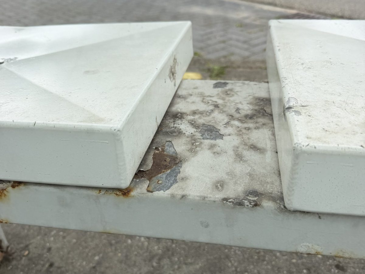 Afbladderende coating met grijs zink eronder op het frame tussen de twee zitjes van het bankje