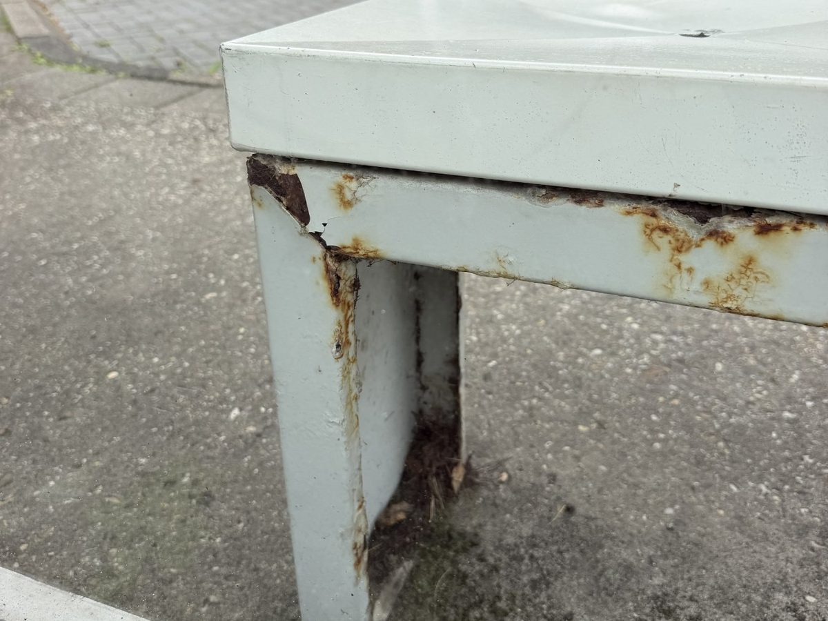 Roest, blaarvorming en afbladderende coating vanuit de randen van het stalen bankje
