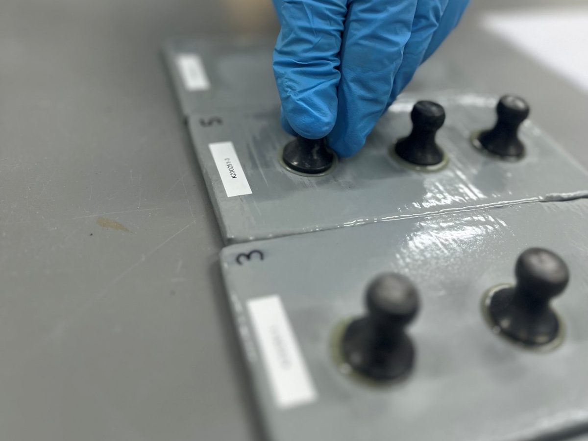 Hand met blauwe handschoen bij dolly's die op grijs gecoate testplaten zijn gelijmd