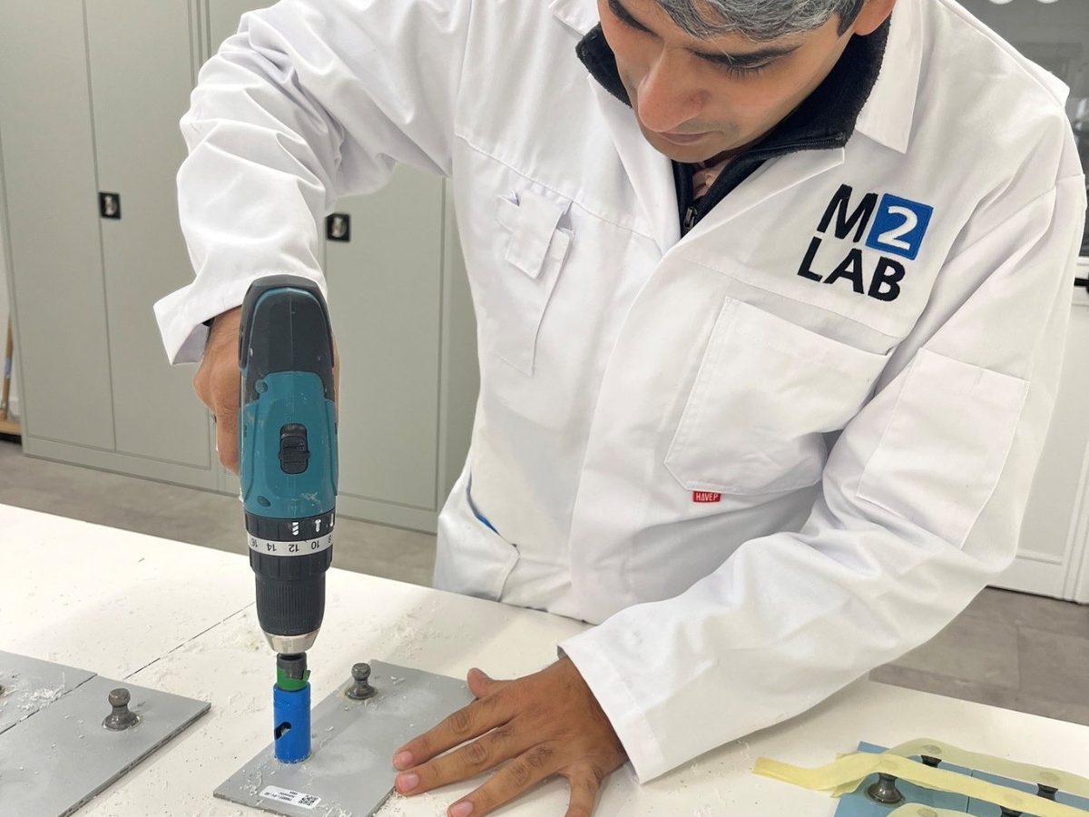 Laborant in M2LAB-labjas snijdt met een boormachine de coating rond een dolly op een testplaat in