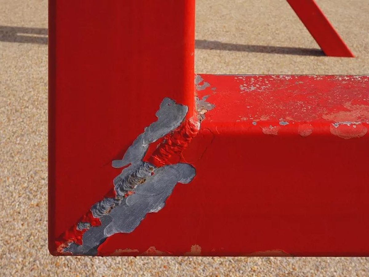Rood gecoat stalen frame waarvan de coating bij een hoek in grote stukken is losgekomen