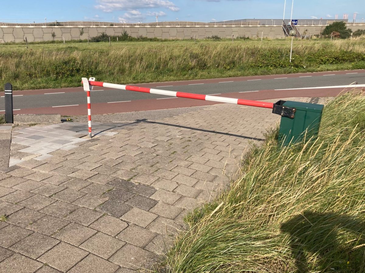 Rood-witte slagboom met groene behuizing bij een fietspad aan zee in IJmuiden