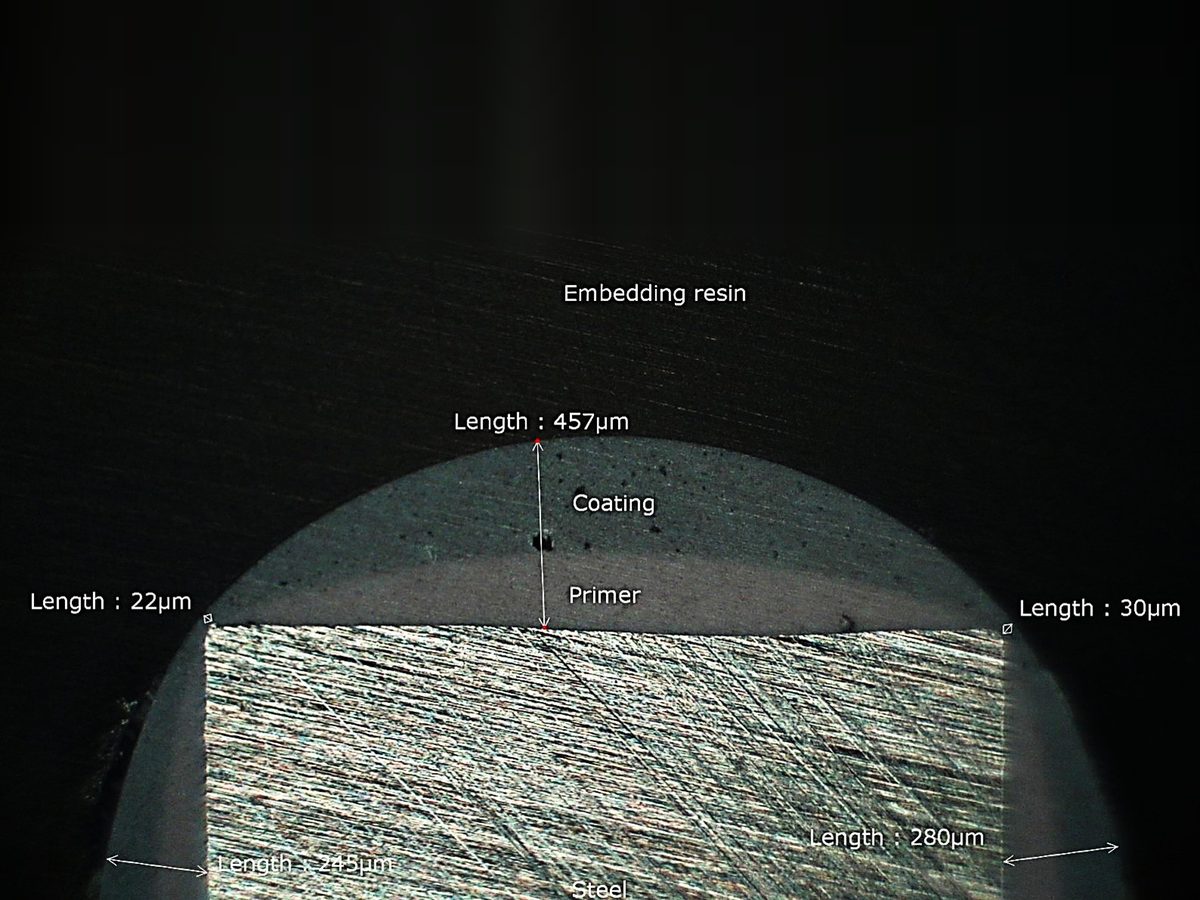 Microscopische doorsnede van een gecoat stalen profiel: 457 µm coating op het vlak, slechts 22 en 30 µm op de scherpe hoeken