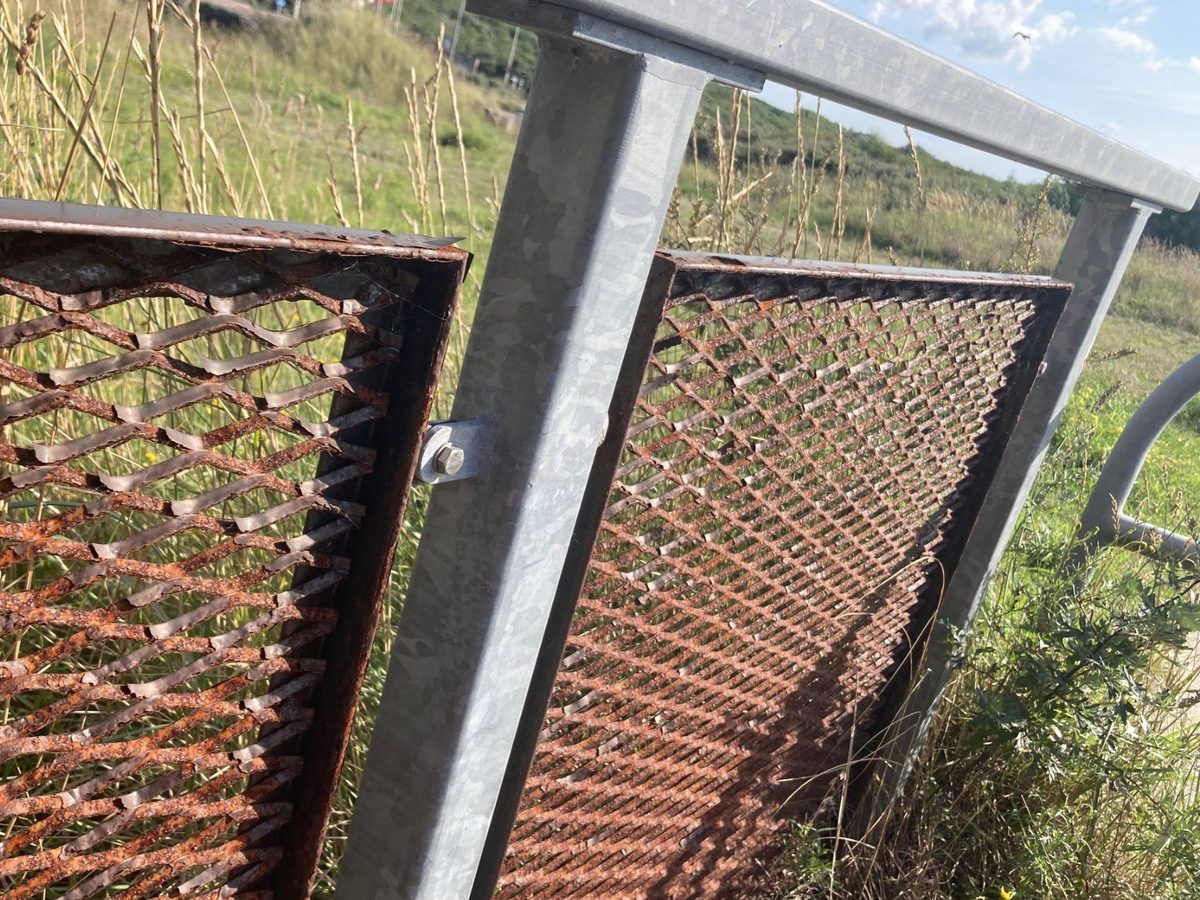 Thermisch verzinkte staander en leuning in uitstekende staat naast verroeste strekmetalen invulpanelen