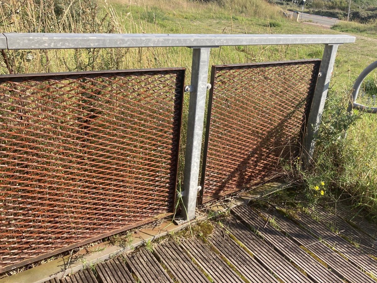 Balustrade naast een trap in IJmuiden: verzinkt frame met bruin verroeste strekmetalen invulpanelen