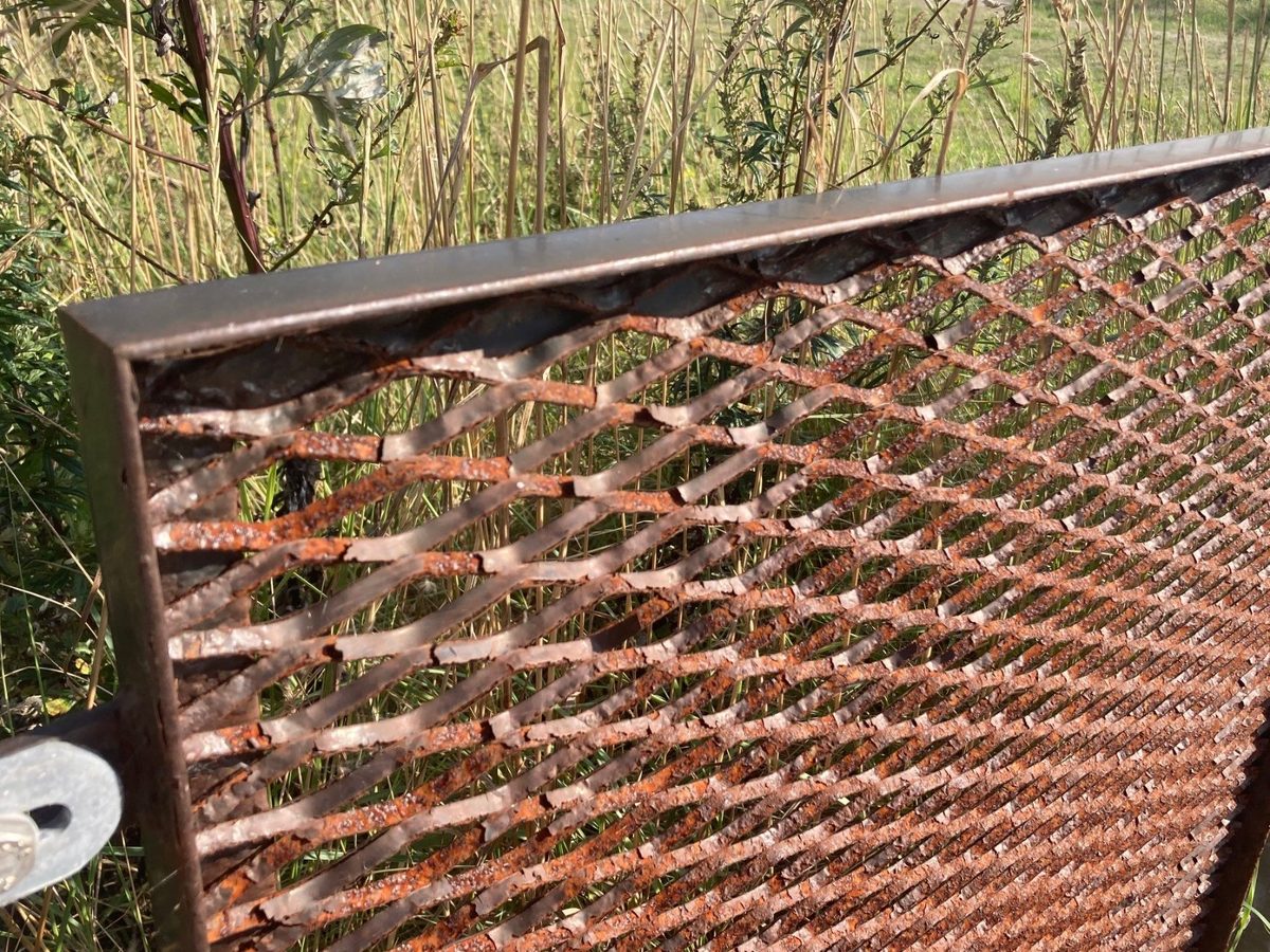 Strekmetalen invulpaneel met afgebladderde coating en roest, ook op het kader eromheen