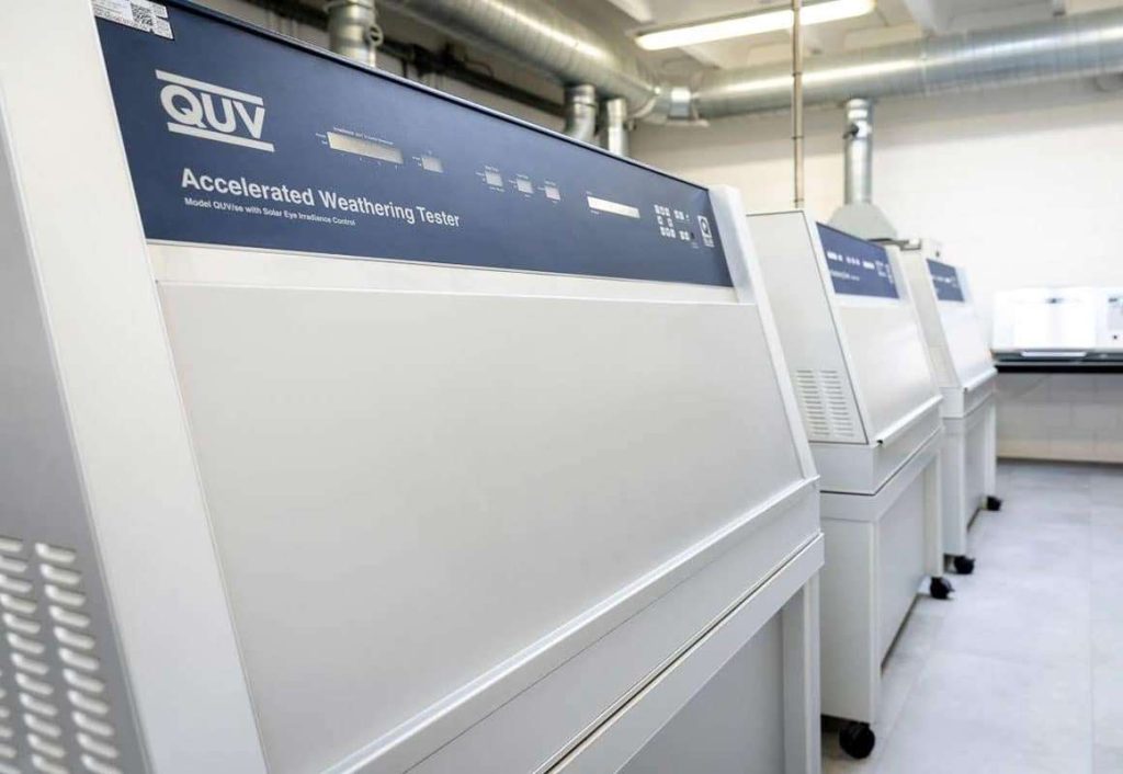 Stralende zon boven twee foto's uit het lab: een rij verweringskasten en een laborante die een testpaneel meet